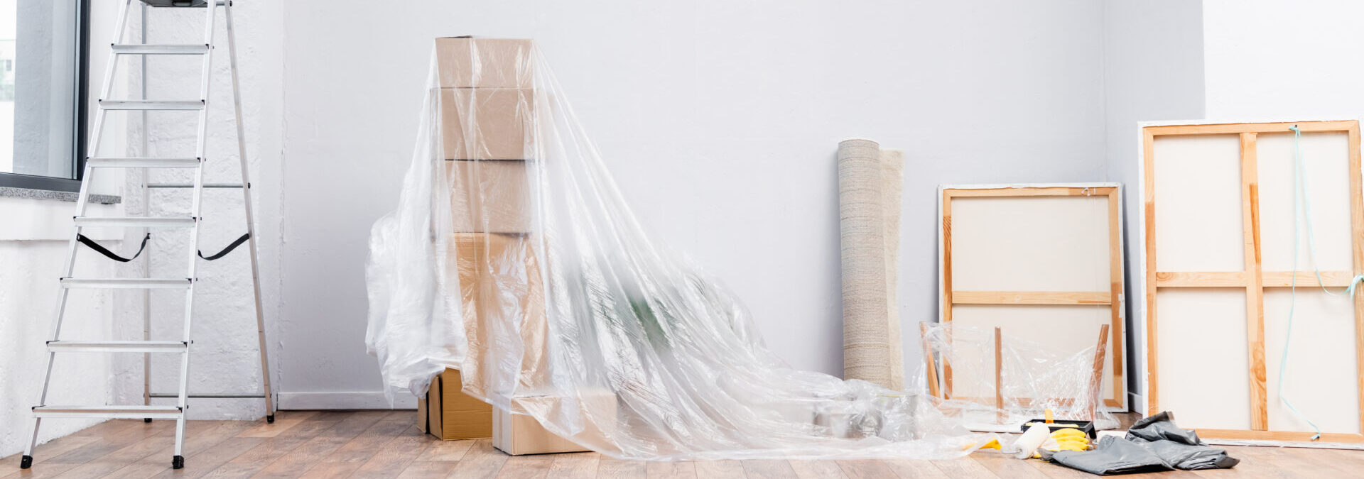 Interior Of Room With Ladder, Cardboard Boxes Covered With Polyethylene, Pictures And Equipment For Repair